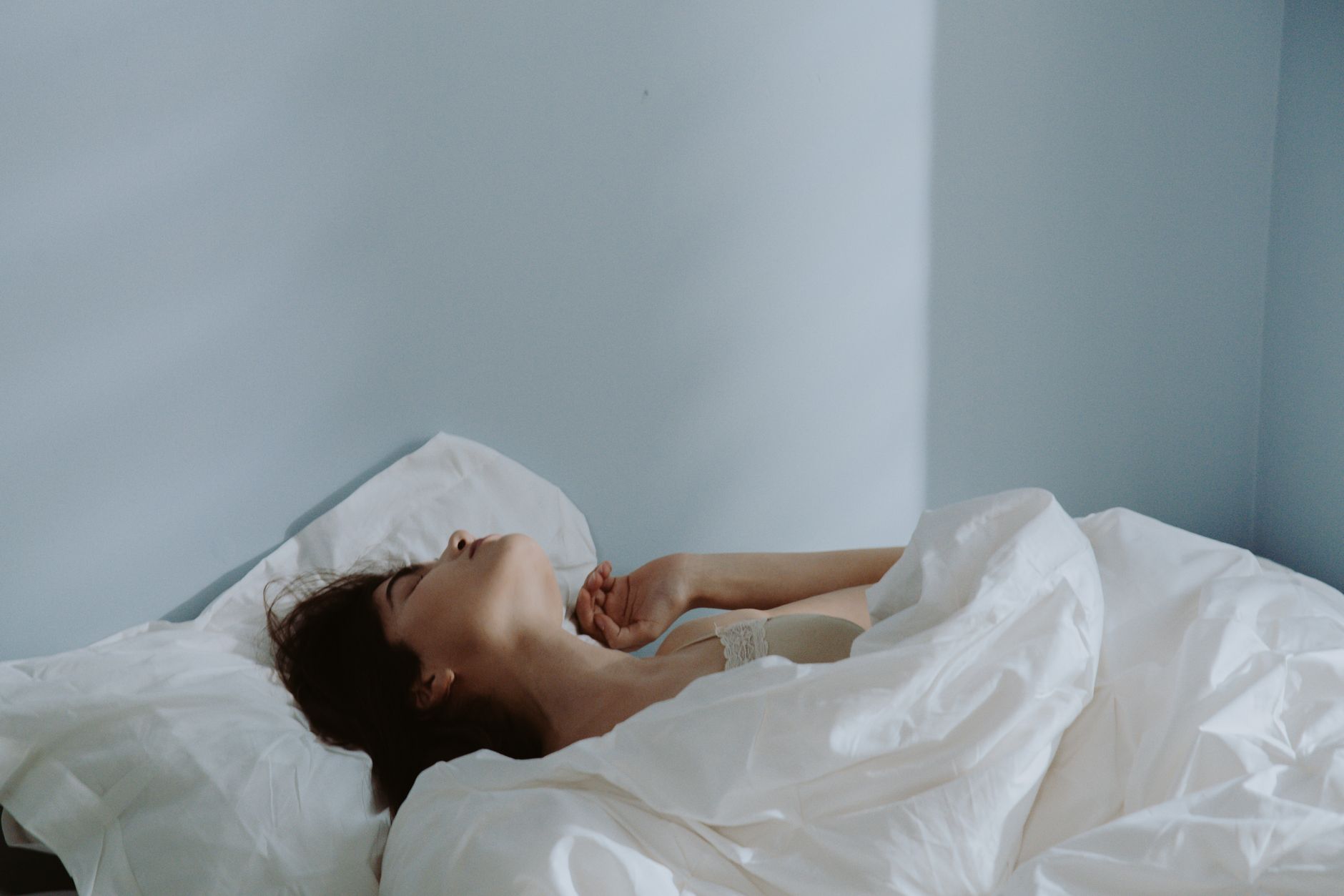 Peaceful scene of a woman sleeping in a soft bed with white linens indoors.