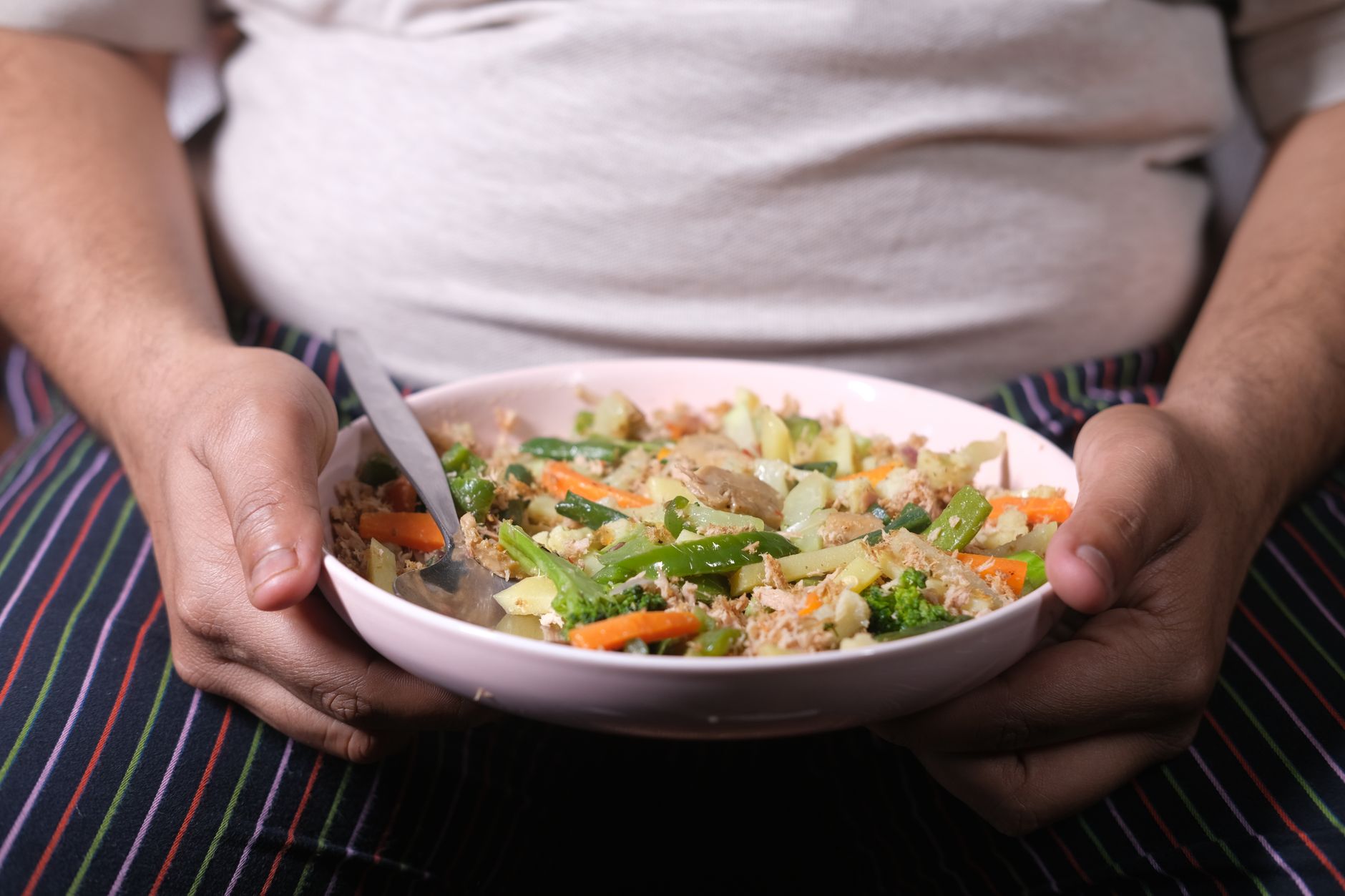 Close-up of an overweight individual holding a nutritious vegetable salad in a pink bowl.