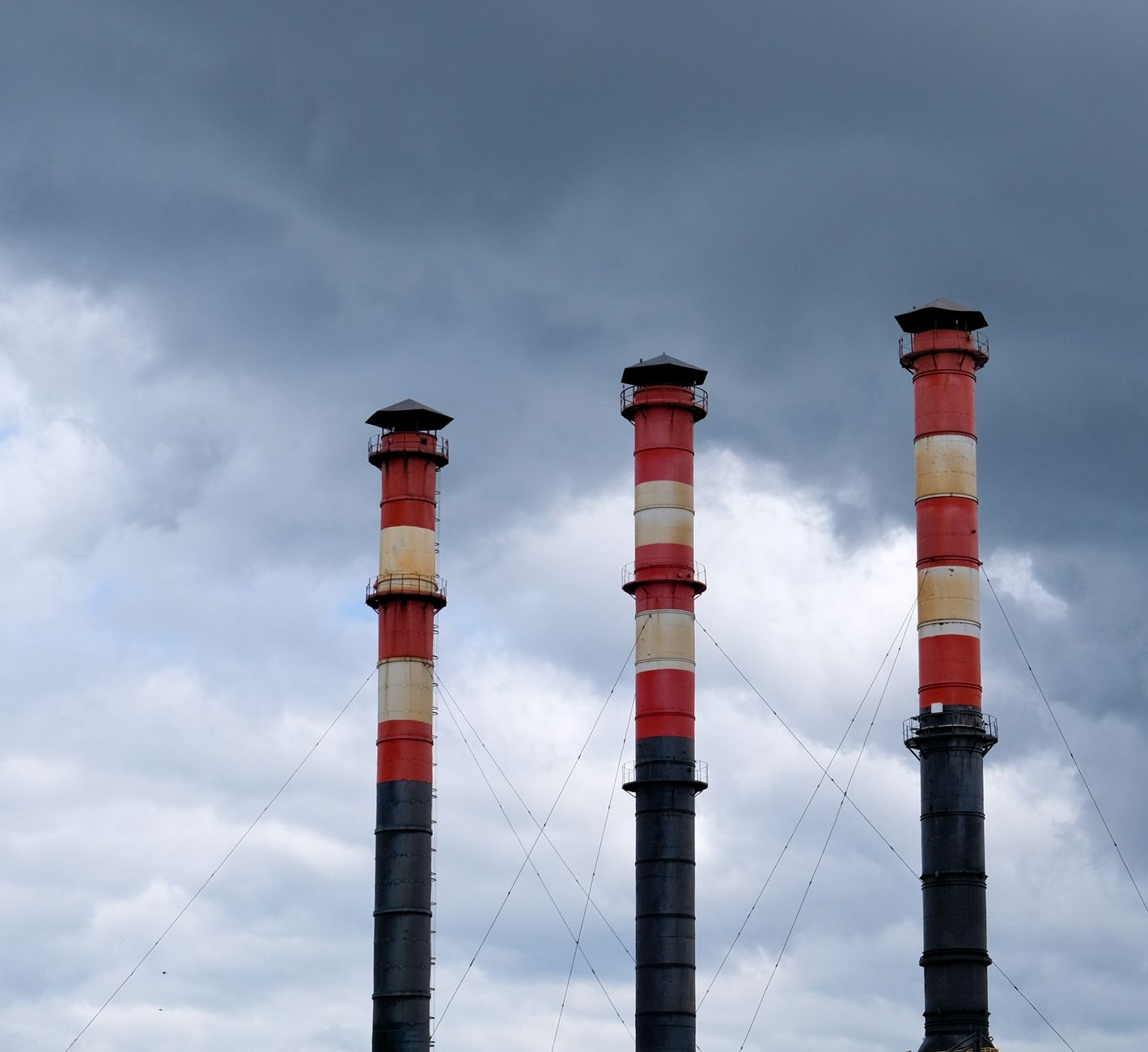 Three tall industrial chimneys stand against a cloudy sky in Minsk, Belarus, highlighting urban pollution issues.