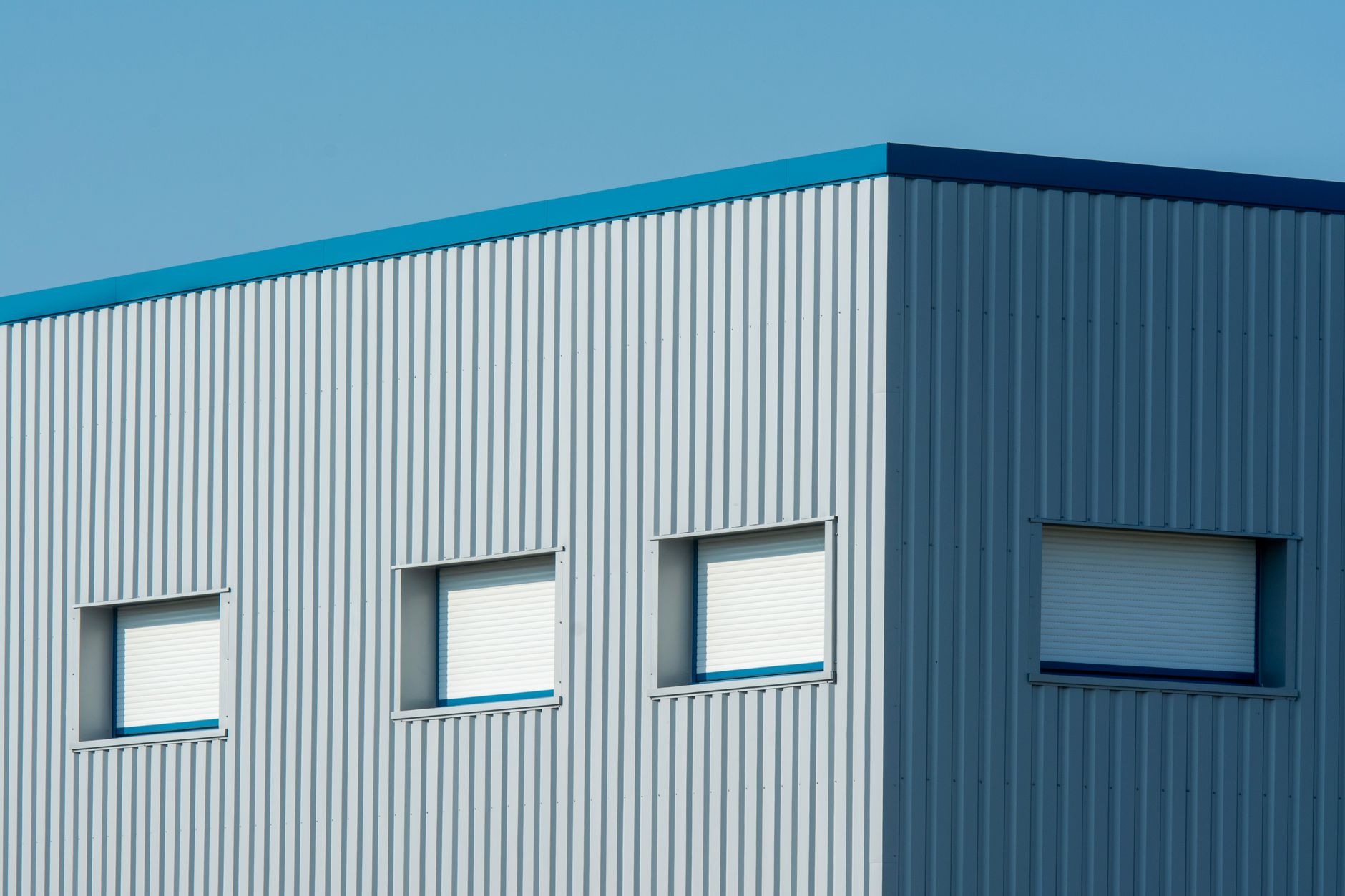 A sleek industrial building with a corrugated metal facade featuring roller blinds and sandwich panels.