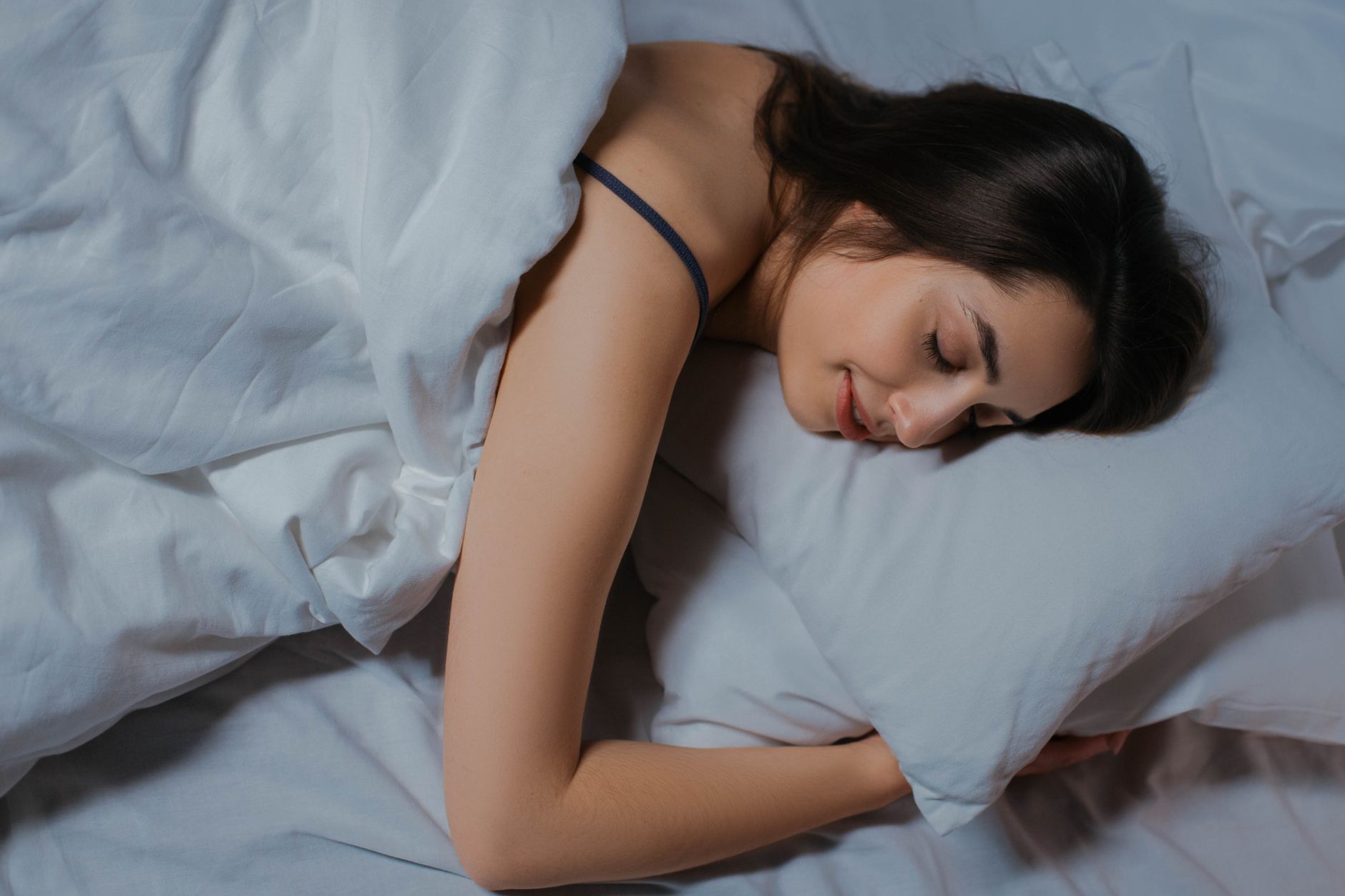 Serene young woman sleeping in cozy bed with white linens. Peaceful and relaxed.