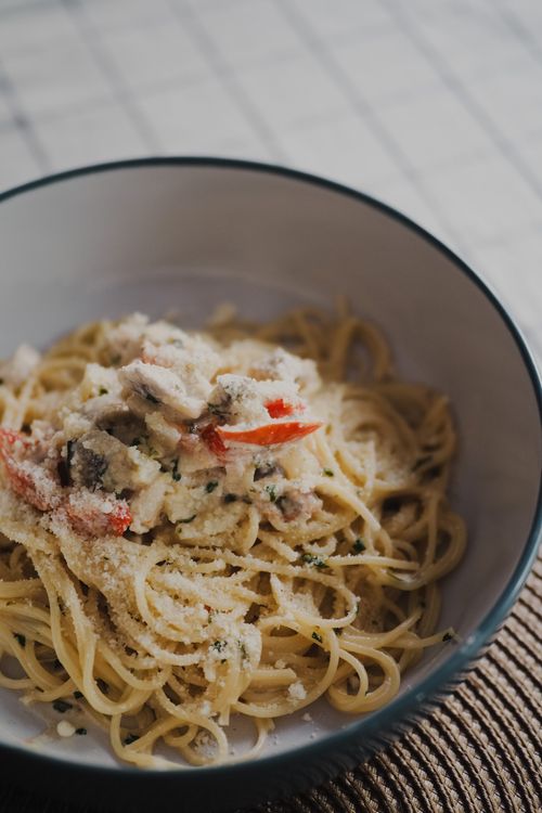 Free A delicious bowl of creamy pasta topped with mushrooms and red peppers, perfect for a cozy meal. Stock Photo
