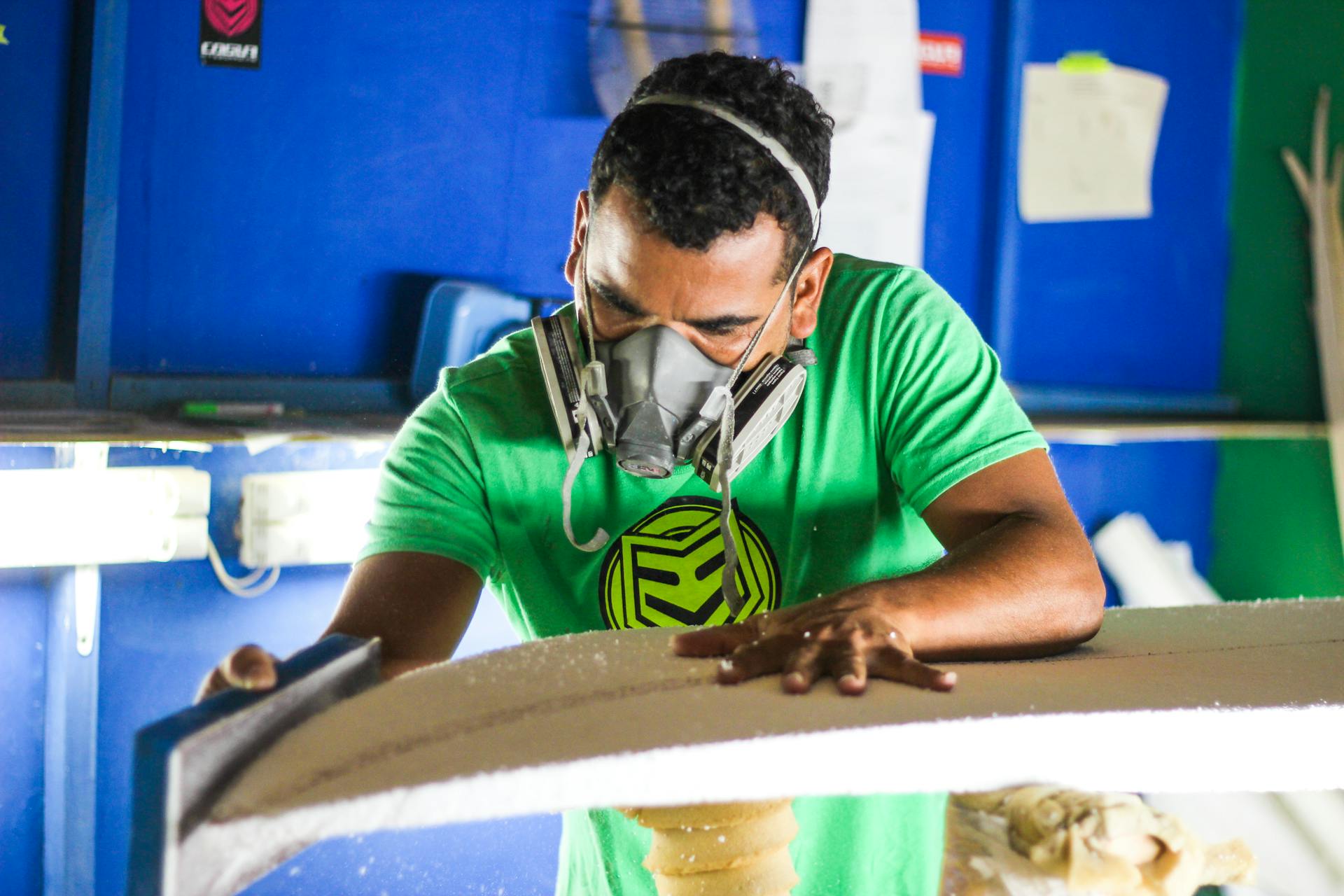 A skilled craftsman in a respirator shaping foam with precision tools in a workshop.