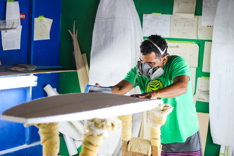 A Man In Green Shirt Shaping A Surfboard