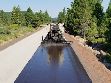 Aerial shot of asphalt paving machine working on a forest road in Oregon, USA.