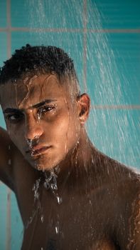 Close-up of a shirtless man showering with water streaming down, against blue tiles.
