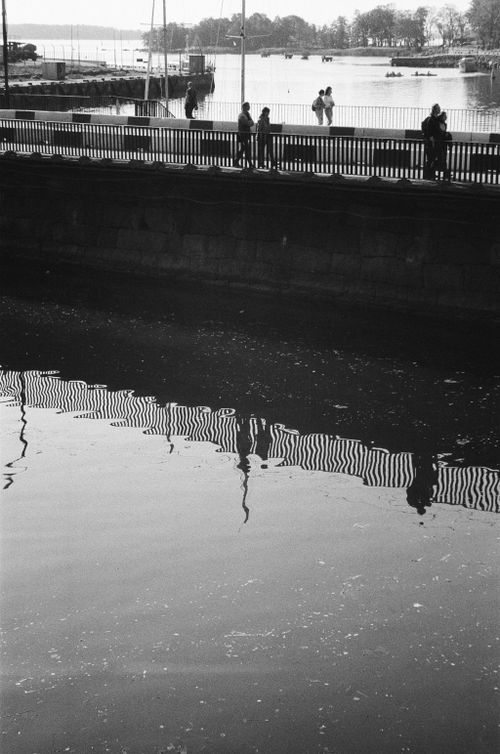 Free A peaceful grayscale scene of people walking by a canal, reflected in water. Stock Photo
