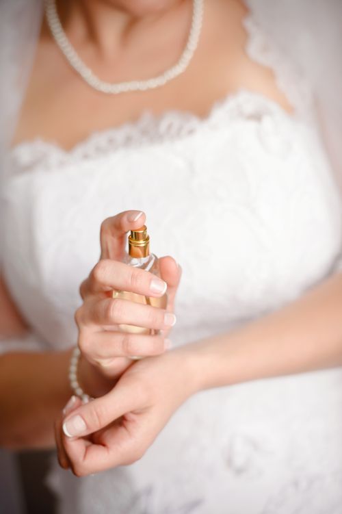 Free Bride in white lace dress applying perfume on wrists, preparing for her wedding day. Stock Photo
