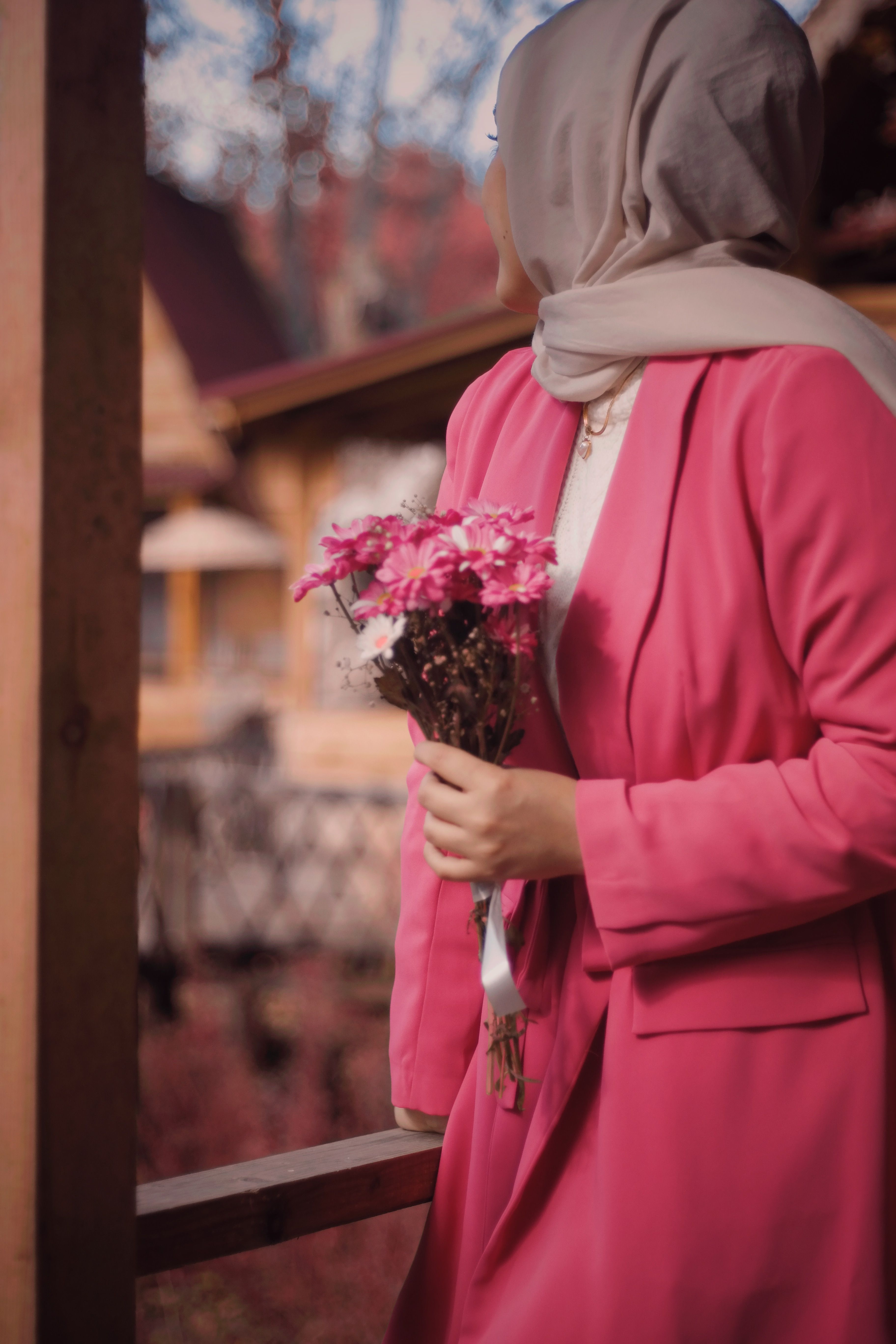 A woman in a pink outfit and hijab holds a bouquet of flowers in an outdoor setting.