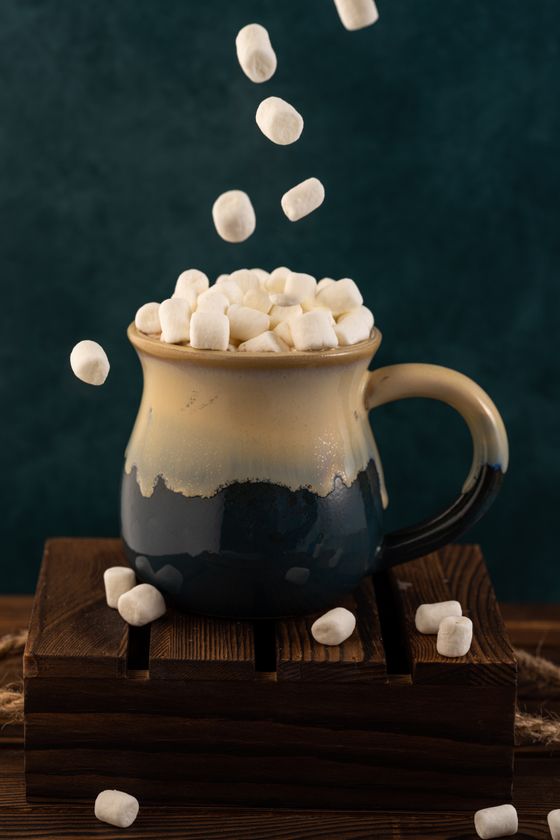 Ceramic mug of hot chocolate heaped with mini marshmallows, more falling from above