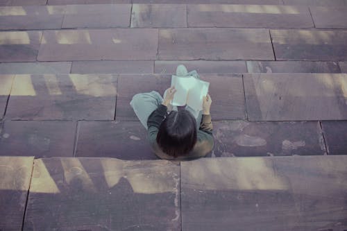 High-Angle Shot of a Person Reading a Book While Sitting on Stairs