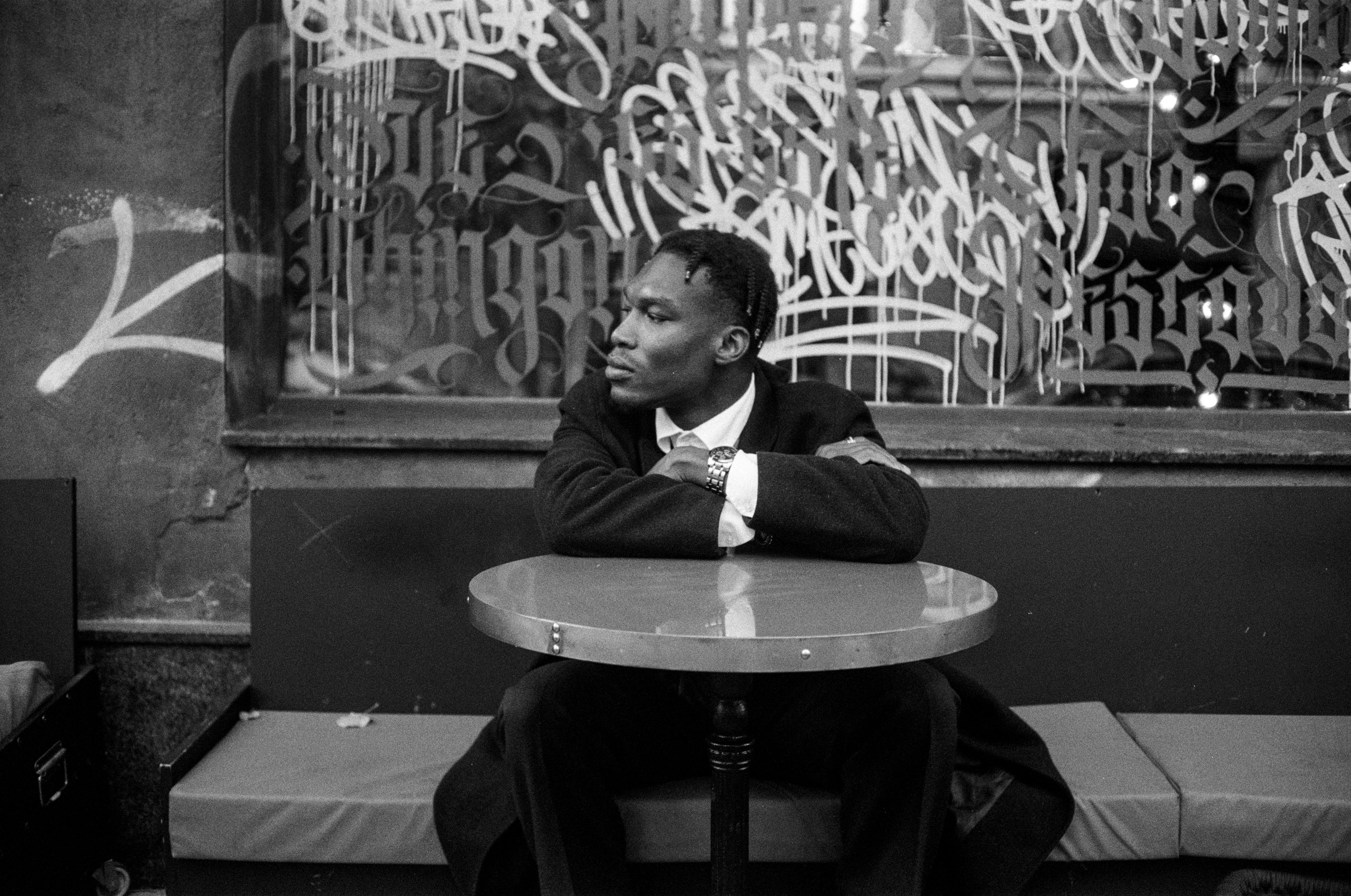 A man in a suit sitting at a round table with graffiti in the background, city vibe.
