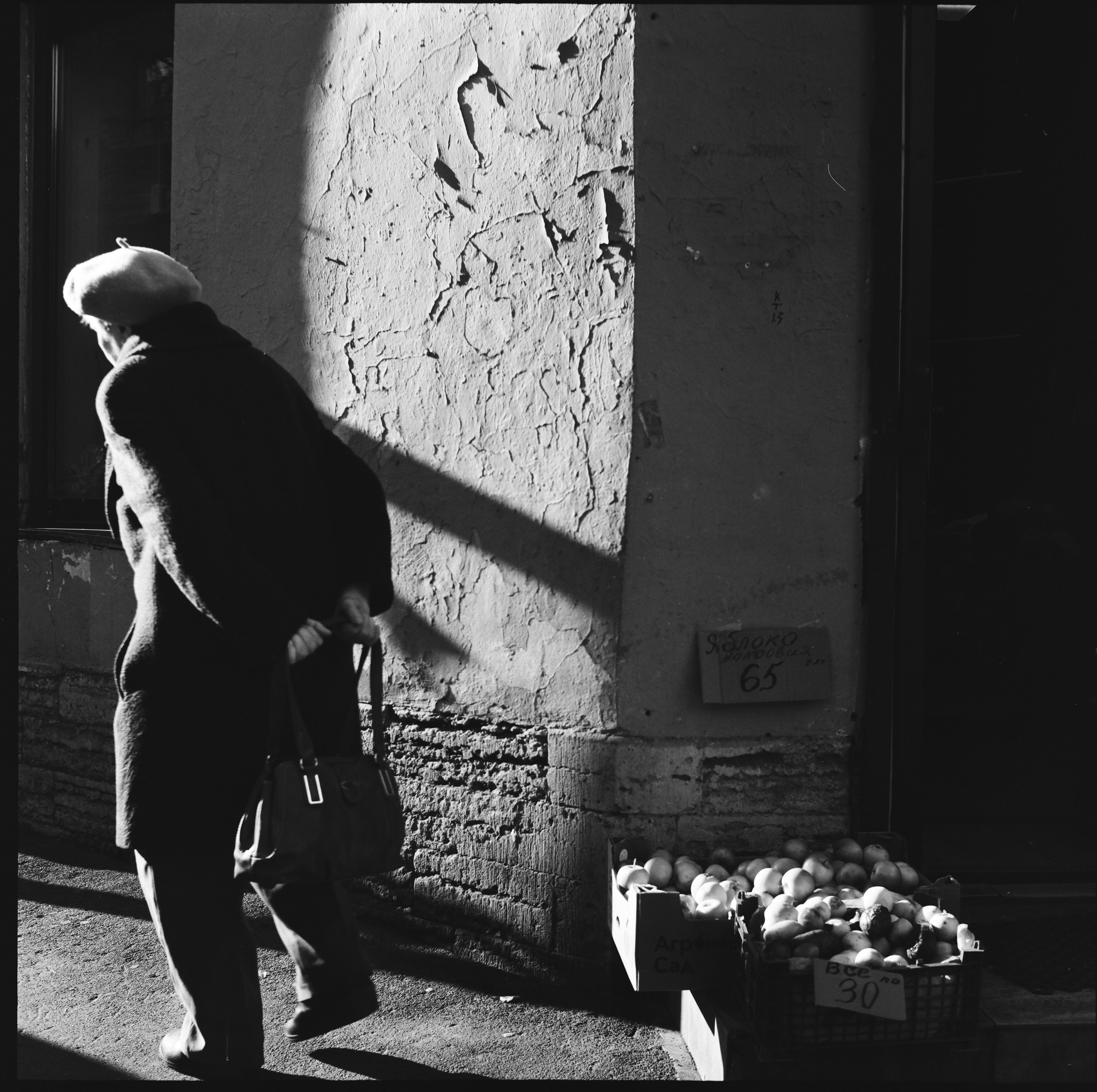 Elderly woman walking past a street market in a black and white urban setting