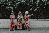 Three Men in Traditional Native American Clothes Playing Guitar on Side of Road