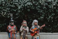 Three Men in Traditional Native American Clothes Playing Guitar on Side of Road