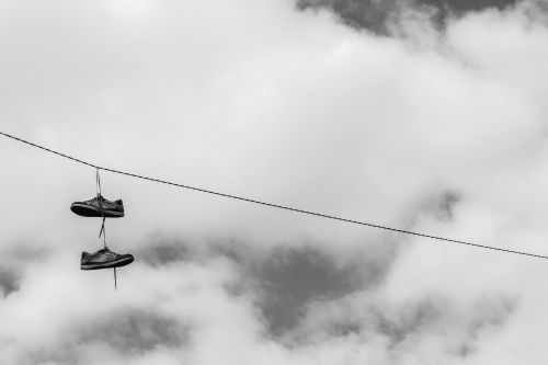 Free Monochrome photo of sneakers hanging from a wire against a cloudy sky. Stock Photo
