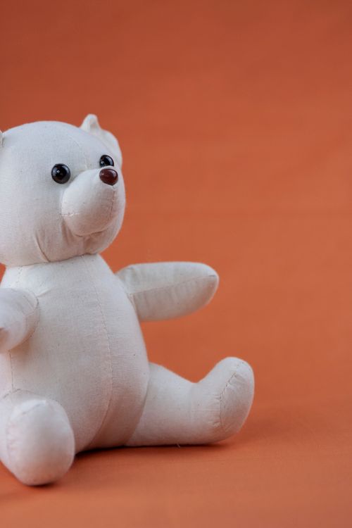 Free Adorable white plush teddy bear sitting on an orange background, perfect for nursery decor or child's gift. Stock Photo