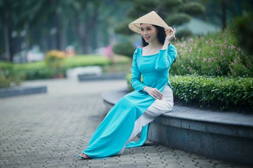 Free Asian woman in Ao Dai and conical hat sitting in a garden setting, embracing traditional culture. Stock Photo