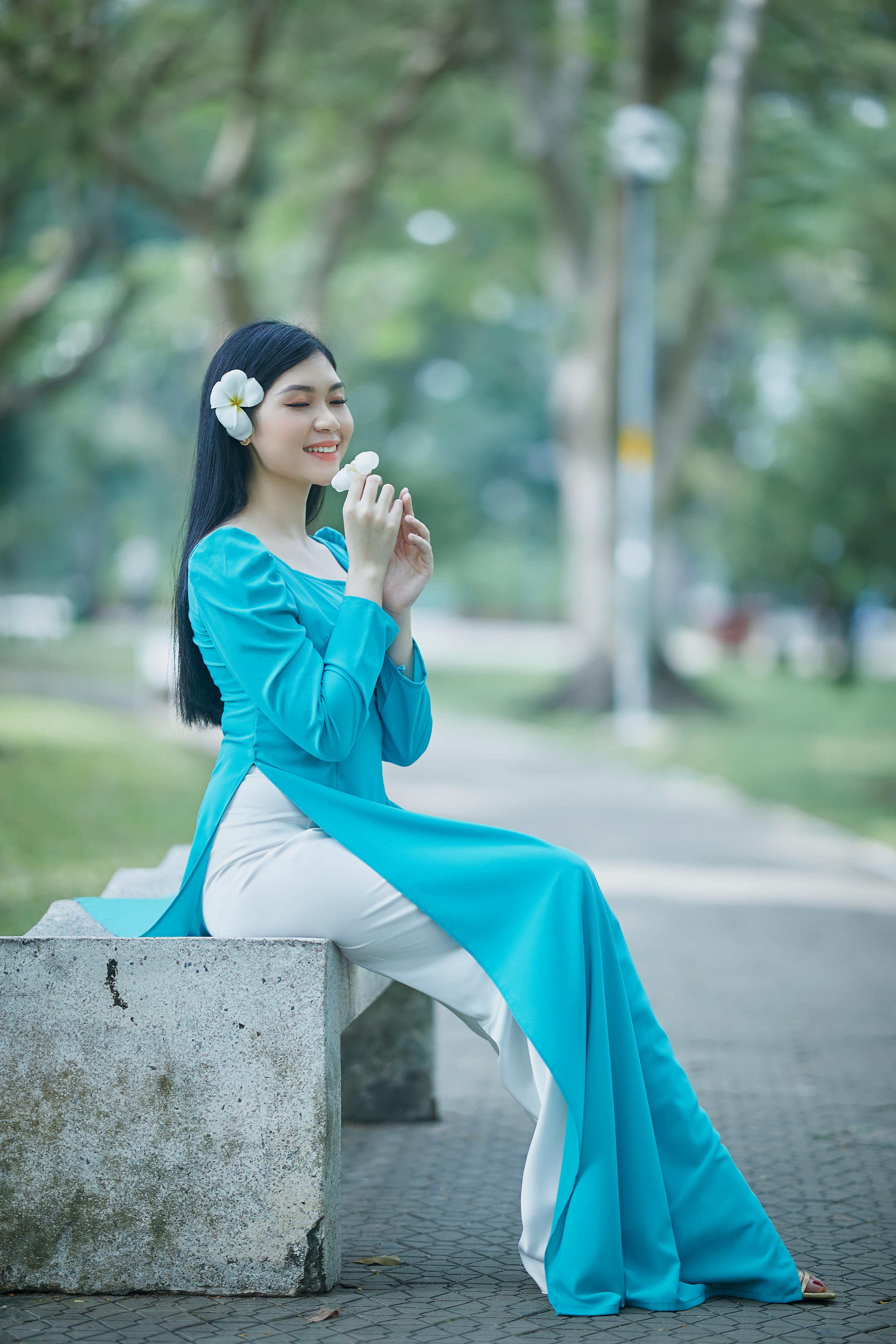 a woman wearing a blue ao dai holding a flower
