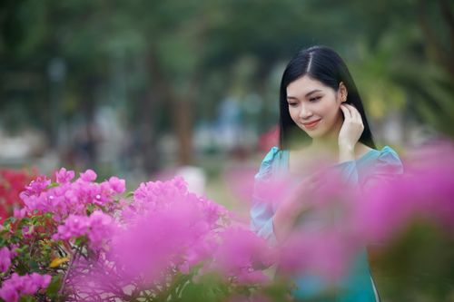 Free Asian woman smiling among bright pink flowers in a lush garden, captured in soft focus. Stock Photo