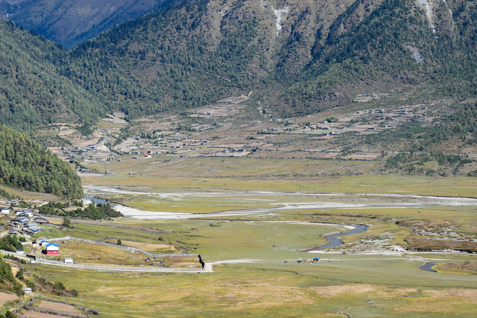 Expansive mountain valley with lush greenery and rural settlements captured during daytime in early autumn.