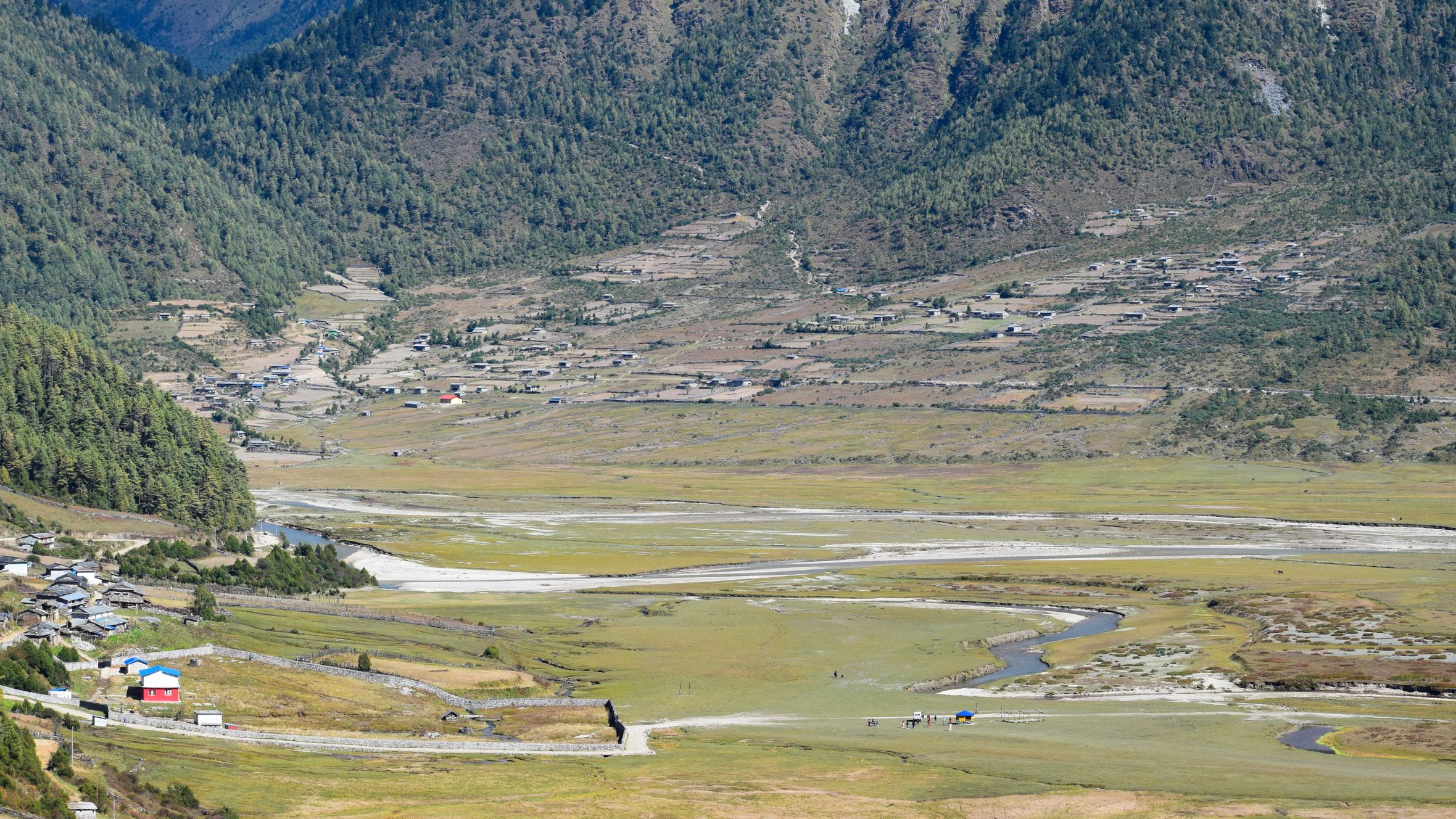 Expansive mountain valley with lush greenery and rural settlements captured during daytime in early autumn.