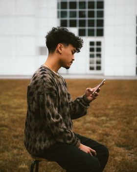 A young adult seated outdoors, engrossed in texting on a smartphone. Casual and modern lifestyle.