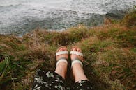 脚穿凉鞋，走在长满草的悬崖边缘，俯瞰着海浪