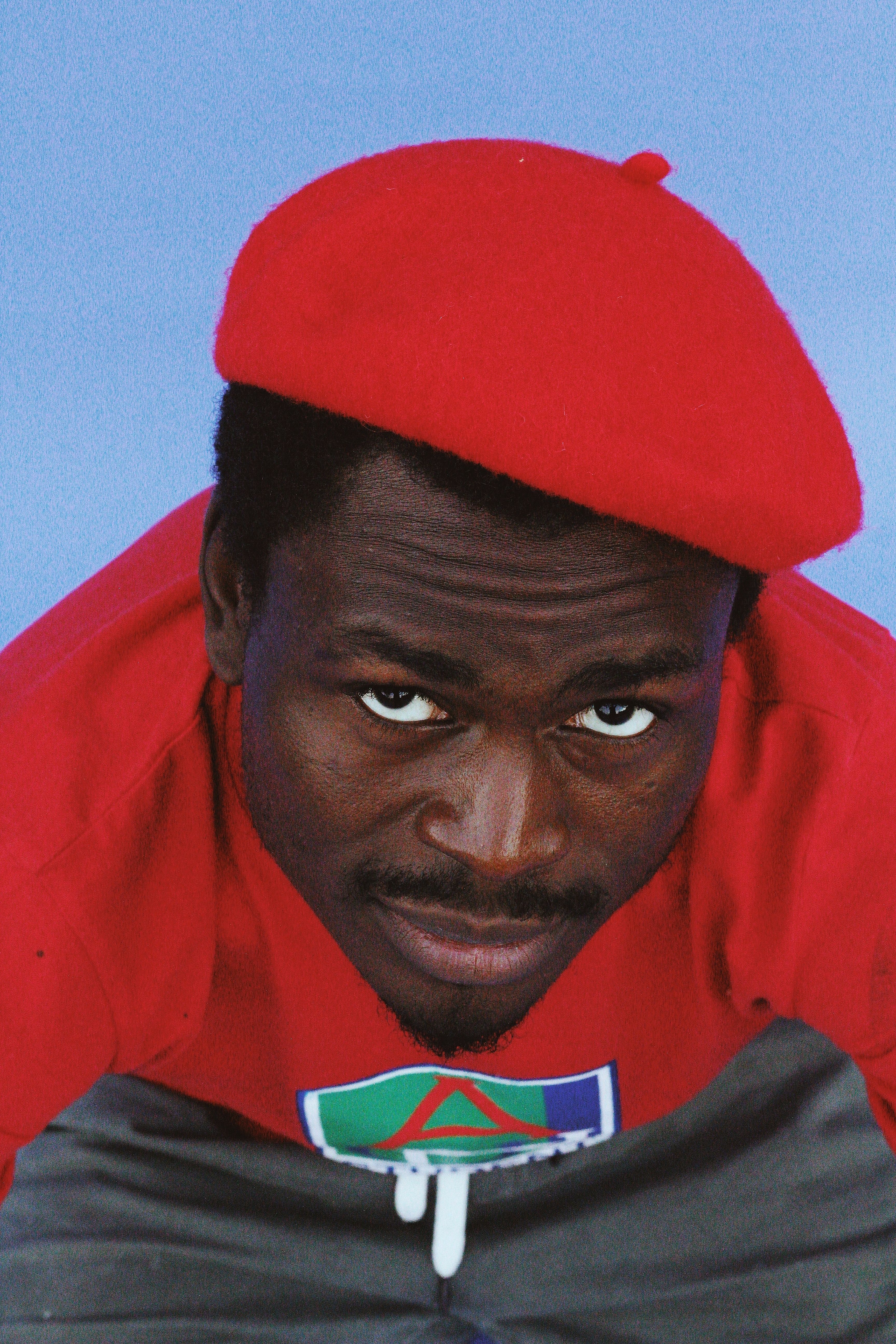 A fashion-forward man in a red beret against a blue background, showcasing style.