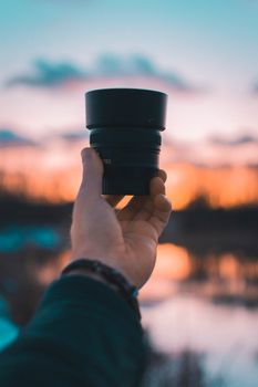 Focused camera lens held against vibrant sunset sky, capturing the essence of photography.