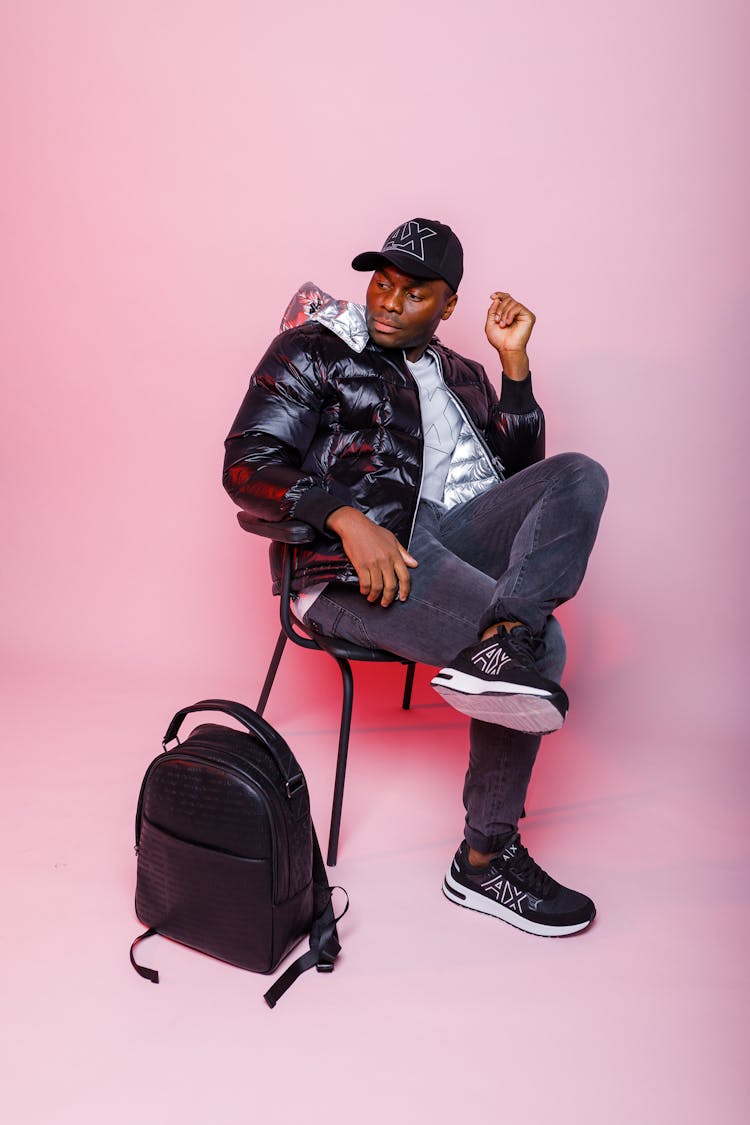 Man In Jacket Sitting On Chair With Bagpack Near