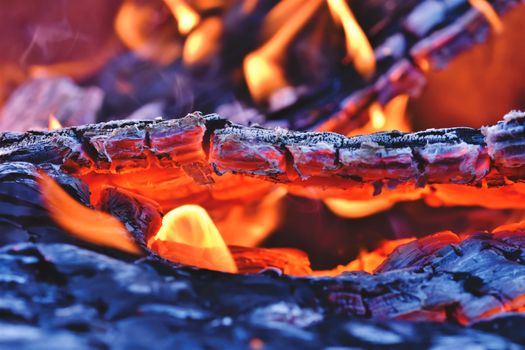 A vibrant close-up of burning wood with glowing embers and intense heat in a fire pit setting.