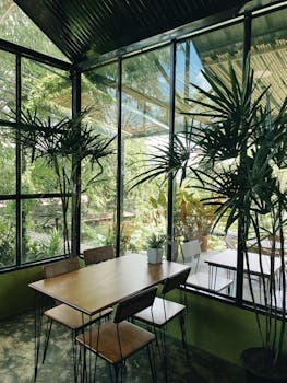 Bright restaurant interior with glass panels and lush plants creating a cozy ambiance.