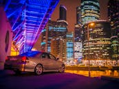 城市场景色彩缤纷，以发光的摩天大楼和一辆停在霓虹灯下的汽车为特色