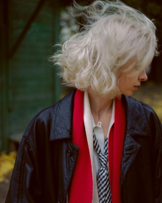 A fashionable woman with blonde hair seen from the side, wearing a black leather jacket and red scarf outdoors.