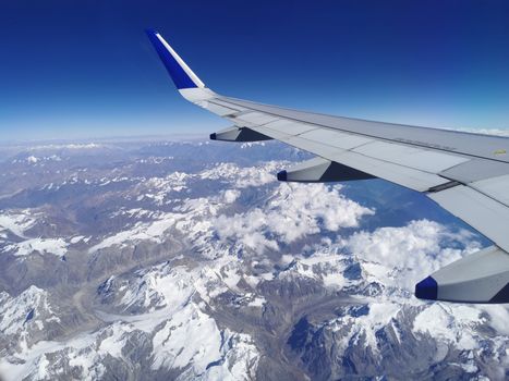 Stunning aerial perspective of the Himalayan mountains with a plane wing in view, showcasing snow-covered peaks and clouds.