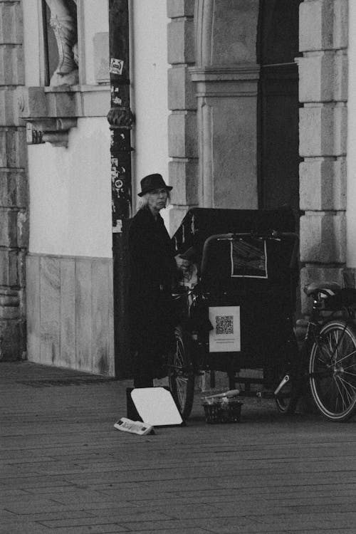 An Elderly Woman Standing on the Street Near the Vehicle