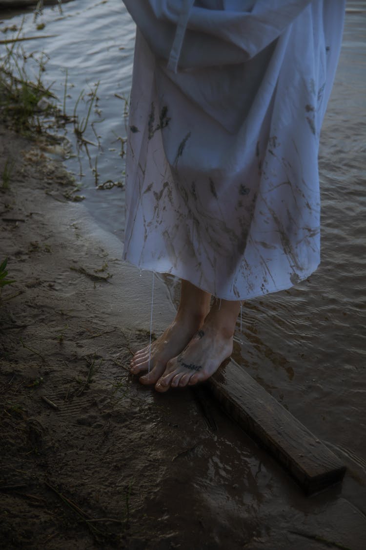 Person In Dirty White Dress Standing Barefoot In Mud On Shore