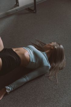 A woman in activewear lying down on an indoor carpeted floor, captured in a serene and relaxed setting.
