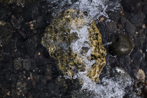 Free Close-up of a large rock on a rocky shore with water splashing over it, highlighting natural textures. Stock Photo