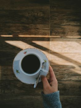 A hand holds a decorative cup of coffee, casting a warm morning shadow.