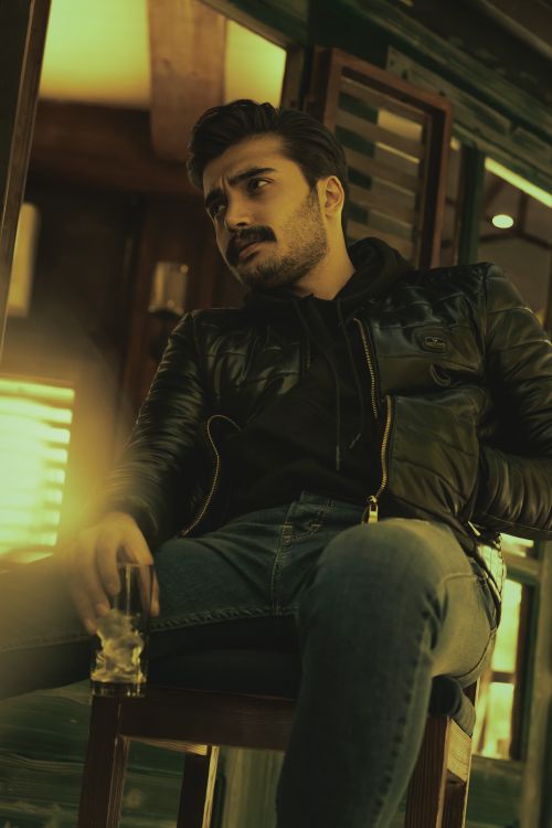 Free Portrait of a man in a black leather jacket sitting indoors with a drink in hand. Stock Photo