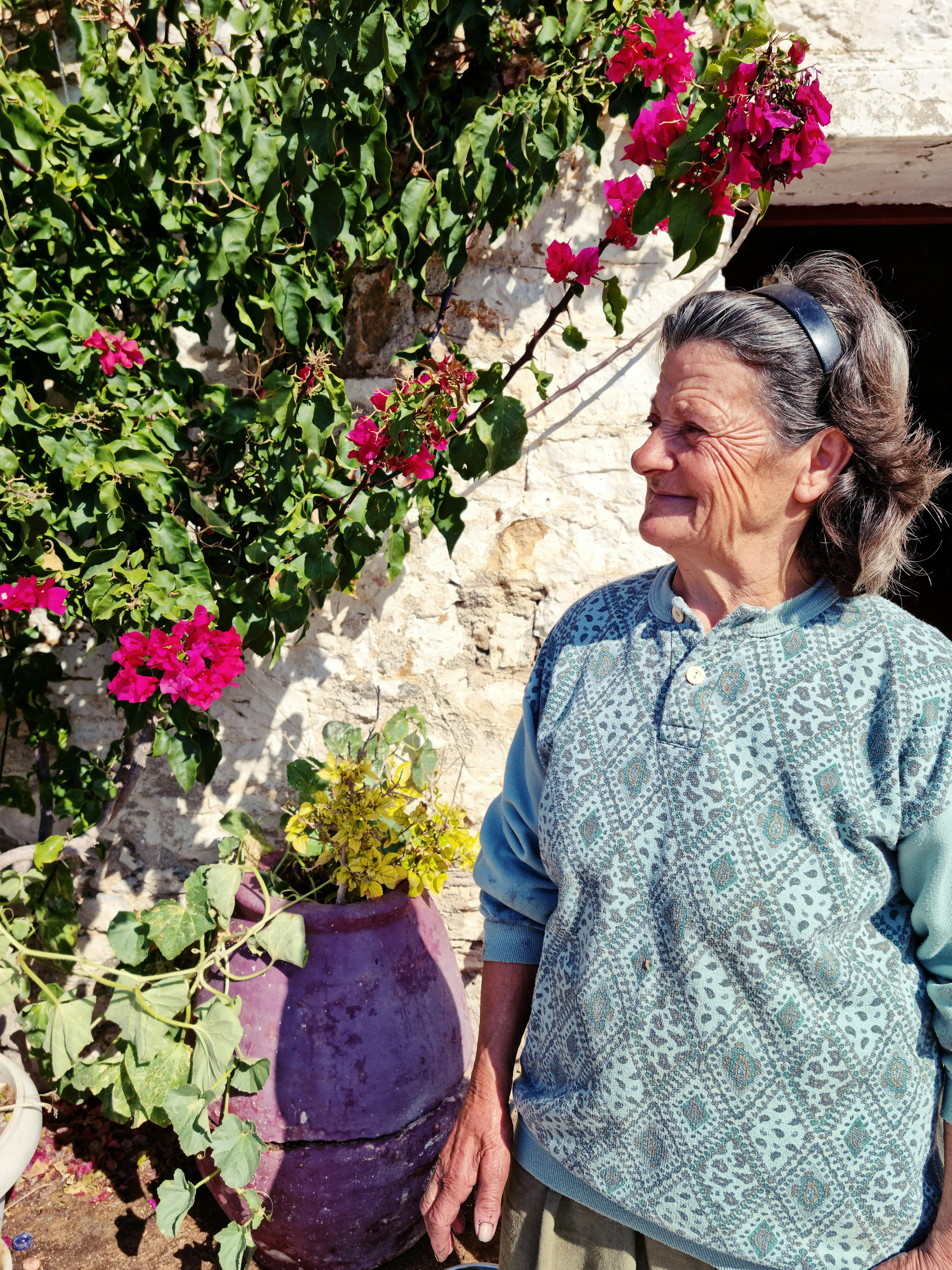 Senior woman smiling among blooming flowers in a sunny garden setting.