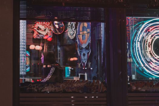 A woman sits in a trendy café illuminated by vibrant neon lights, creating a moody ambiance.