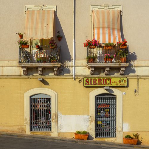 Free Italian storefront facade with colorful balconies displaying vibrant flowers and striped awnings. Stock Photo