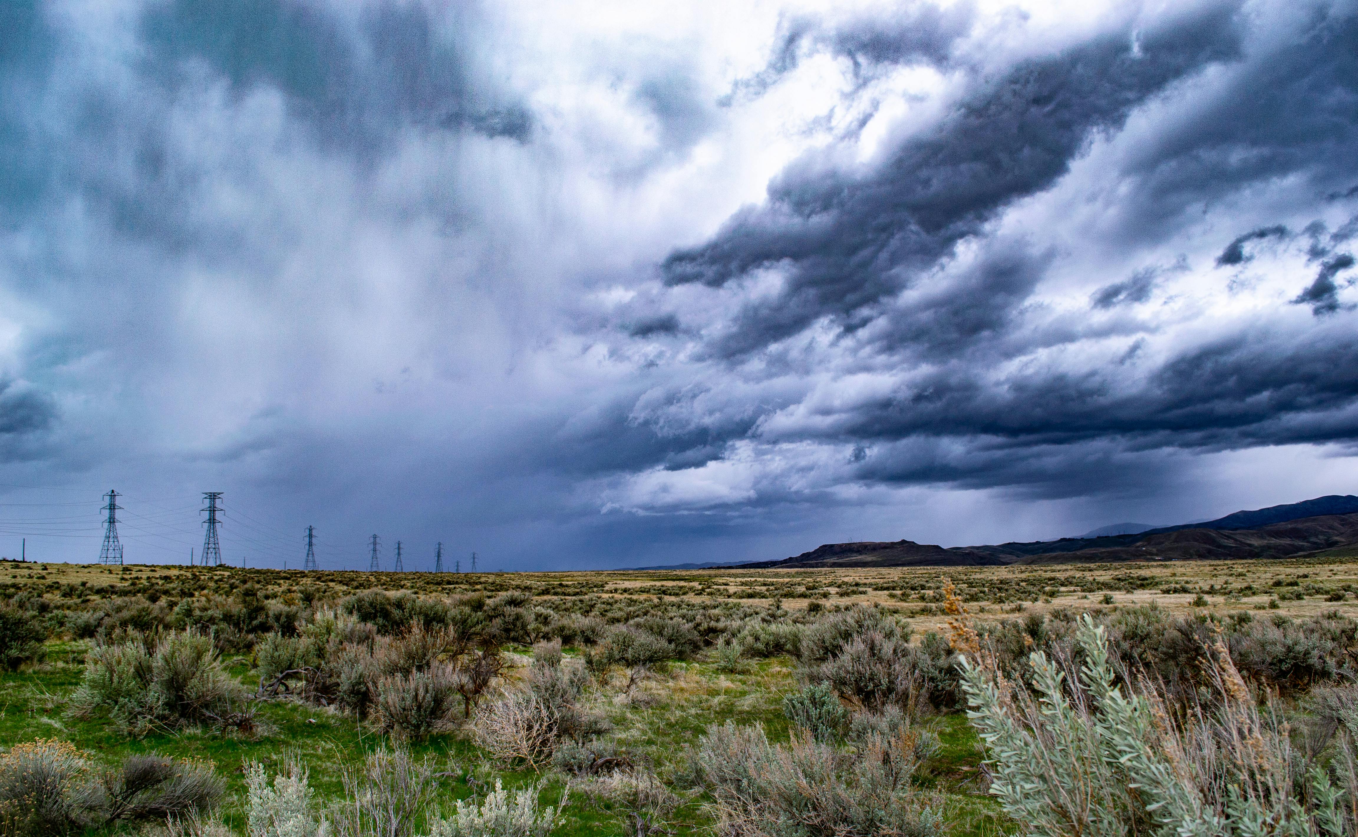 广阔的田野上笼罩着戏剧性的云层，远处是山脉和电力线