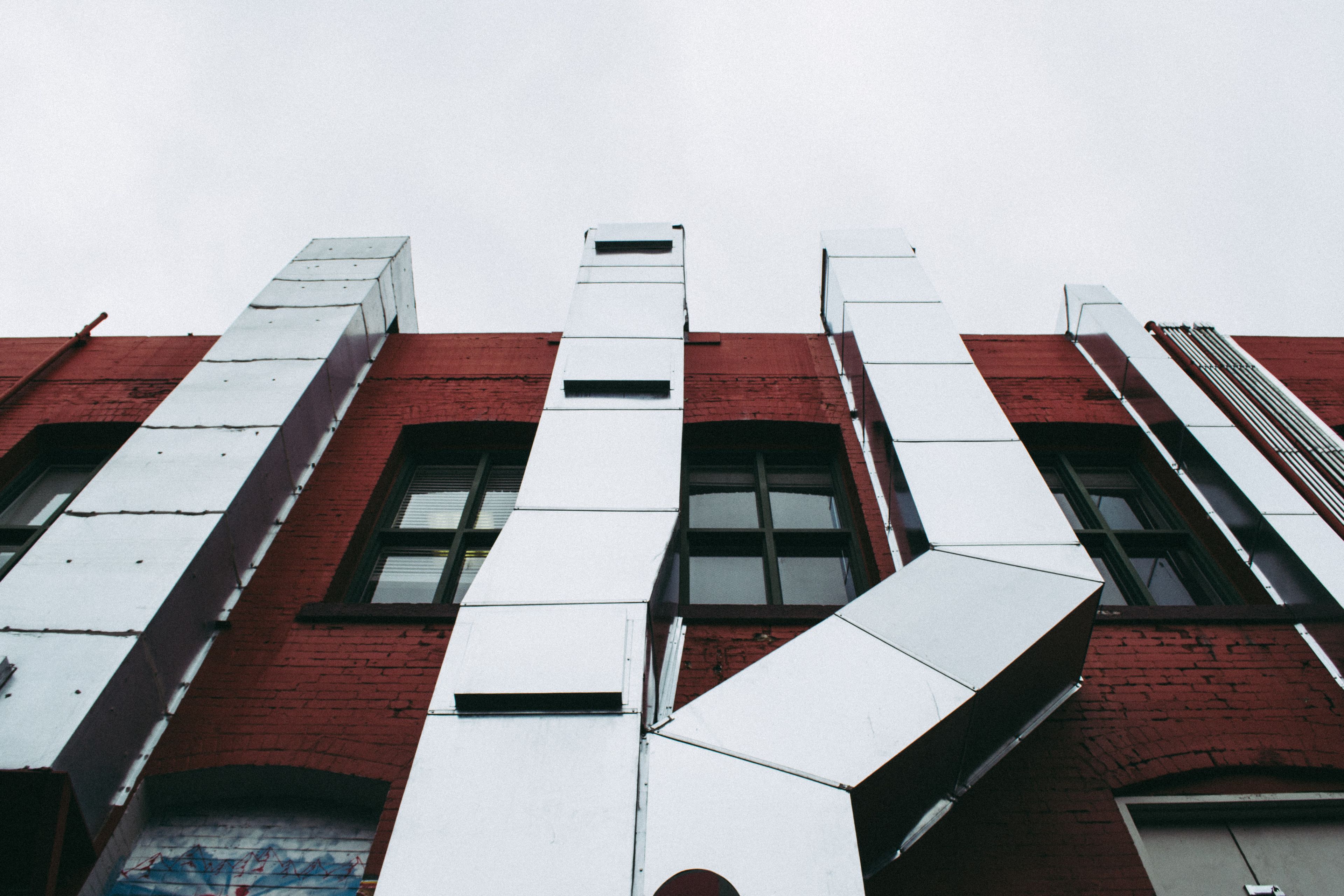 Conduits métalliques d'extraction sur une façade de brique rouge, exposés aux intempéries