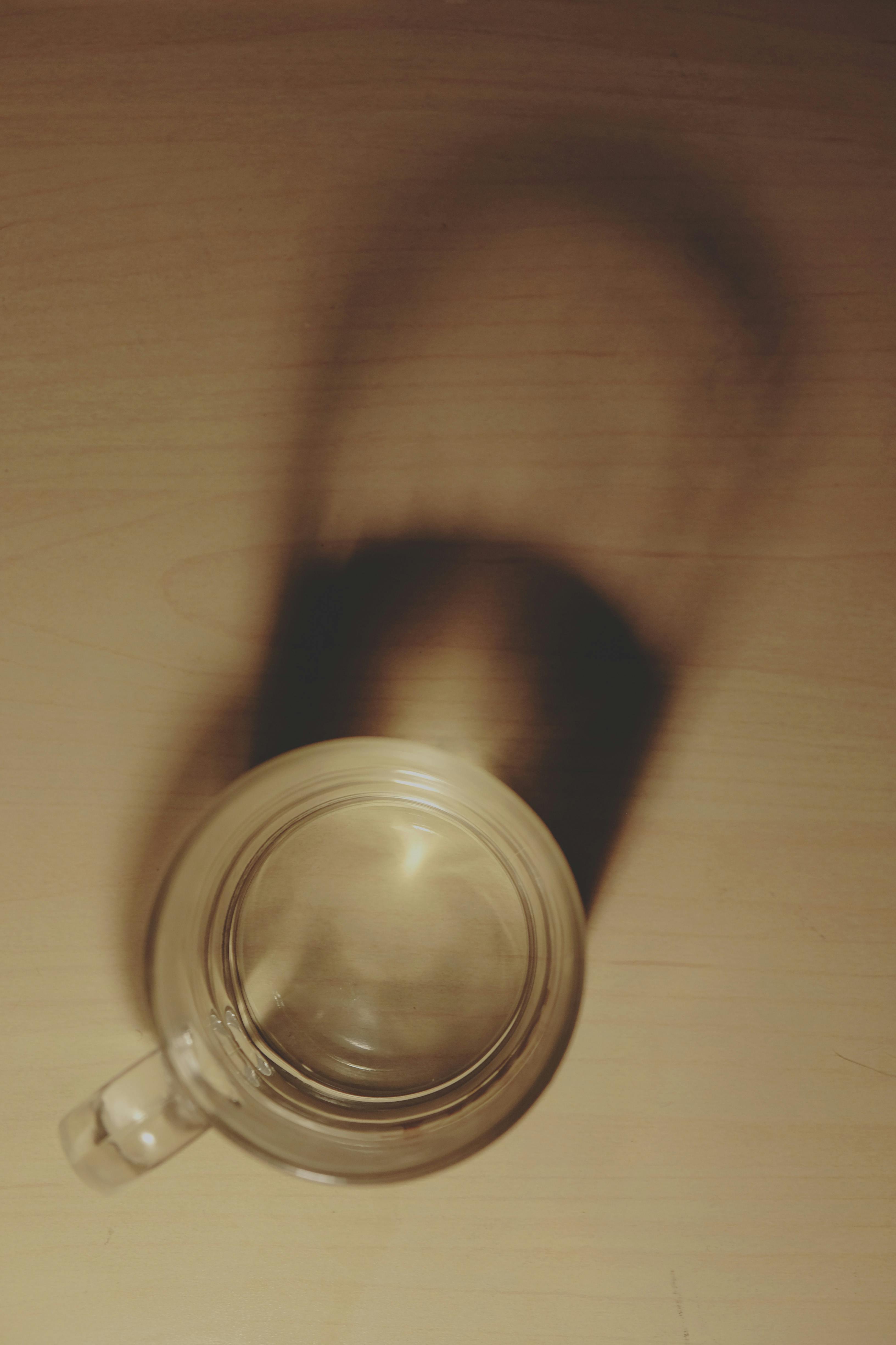 A clear glass mug casting a dramatic shadow on a wooden table, captured in a top view.