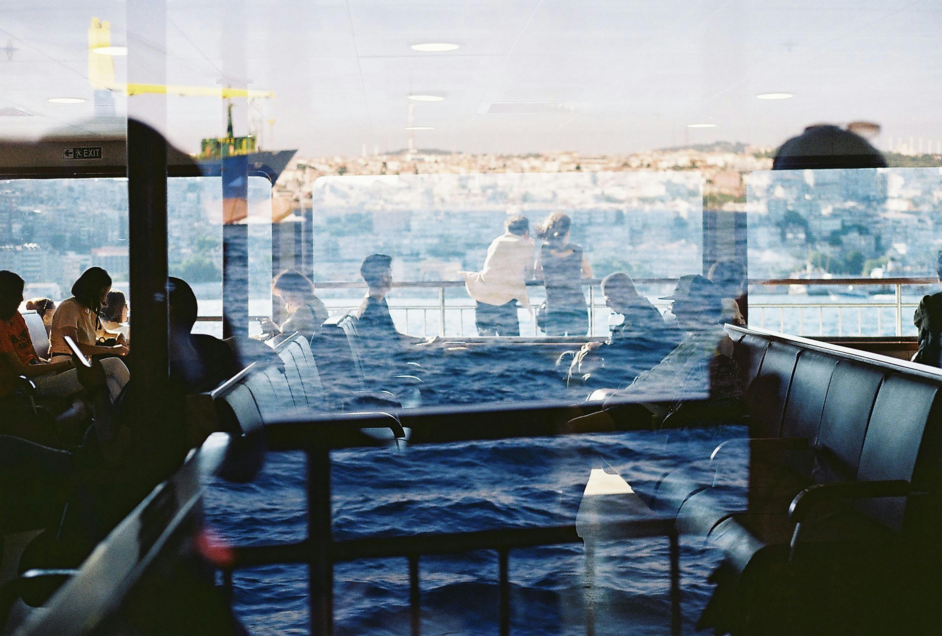 Double exposure of passengers on a ferry with an urban cityscape backdrop.