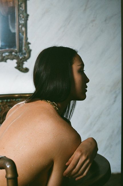 A creative portrait of a woman with long dark hair sitting indoors, captured artistically.